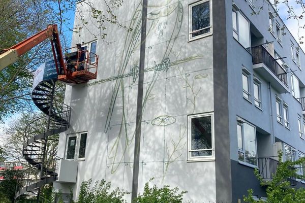 Muurschildering van een vogel wordt op een woongebouw aangebracht
