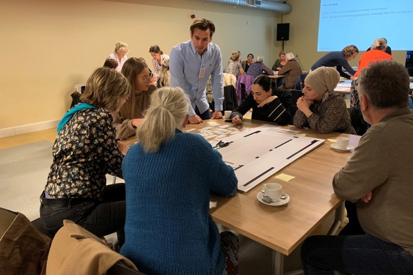 Bewoners zitten samen om tafel met een medewerker van Intermaris en plakken post-its op een poster