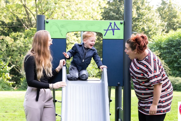 Twee vrouwen staan naast een glijbaan waar een kindje op zit