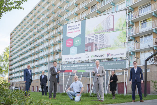 Diverse mensen staan bij het bouwbord voor een woongebouw