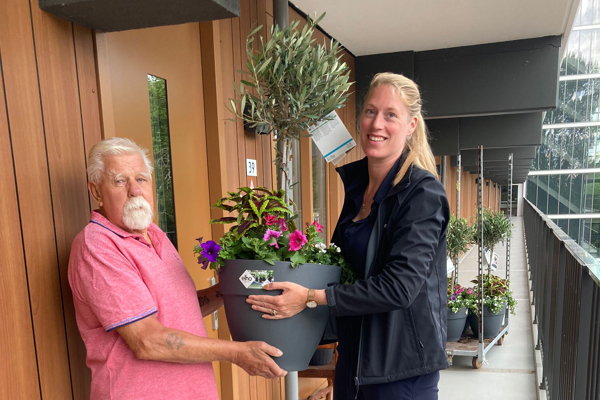 Bewoner ontvangt een boompje in een pot van een medewerker van Intermaris
