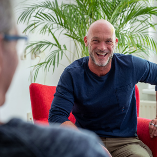 Medewerker van Intermaris zit lachend op een rode stoel in gesprek met een bewoner