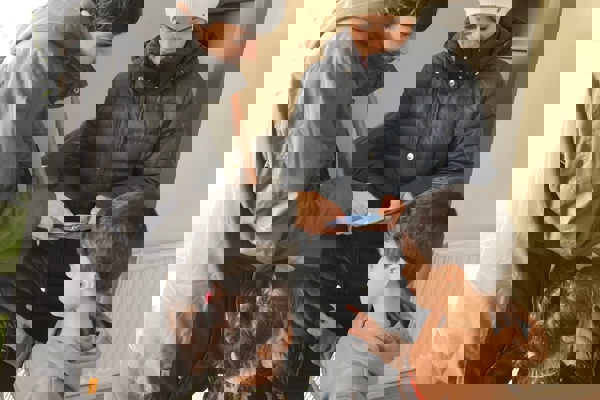 Man geeft uitleg aan een vrouw op haar telefoon met twee kinderen erbij