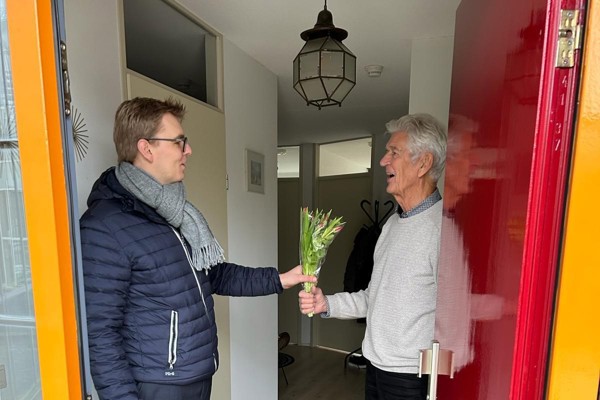 Bewoner ontvangt een bos tulpen van directeur wonen Jurre Terhorst tijdens complimentendag