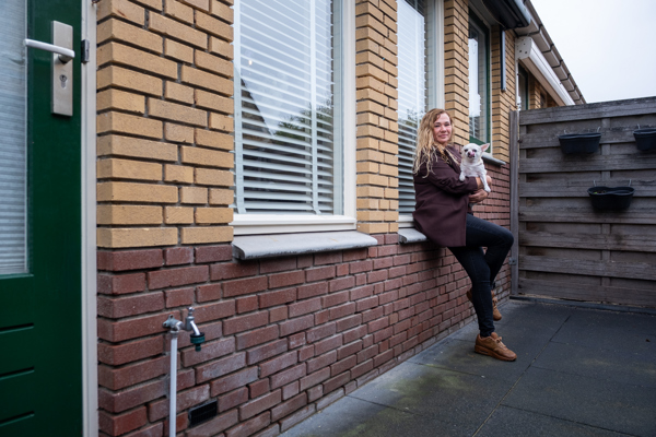 Vrouw zit met haar hond op schoot op de vensterbank voor het raam buiten haar woning.