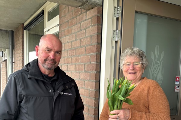 Bewoonster en medewerker Intermaris poseren voor woning met een bos tulpen